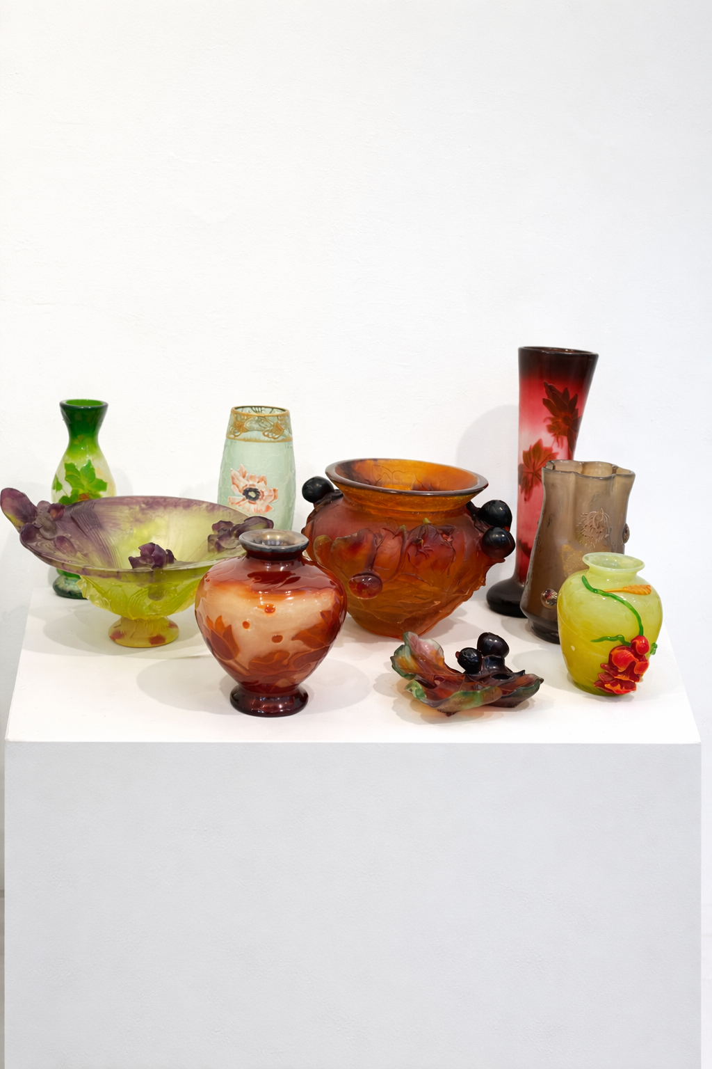 Mehrere farbige Jugendstil Kunstglas Vasen und Schalen auf weißem Sockel vor neutralem Hintergrund – Cameoglas und dekorative Glasobjekte im Stil von Gallé, Daum Nancy, Lötz Wien und Lalique